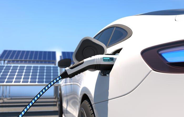 En hvid elbil under opladning med solceller i baggrunden.